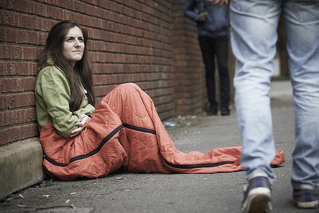 Young woman sits in sleeping bag on the street